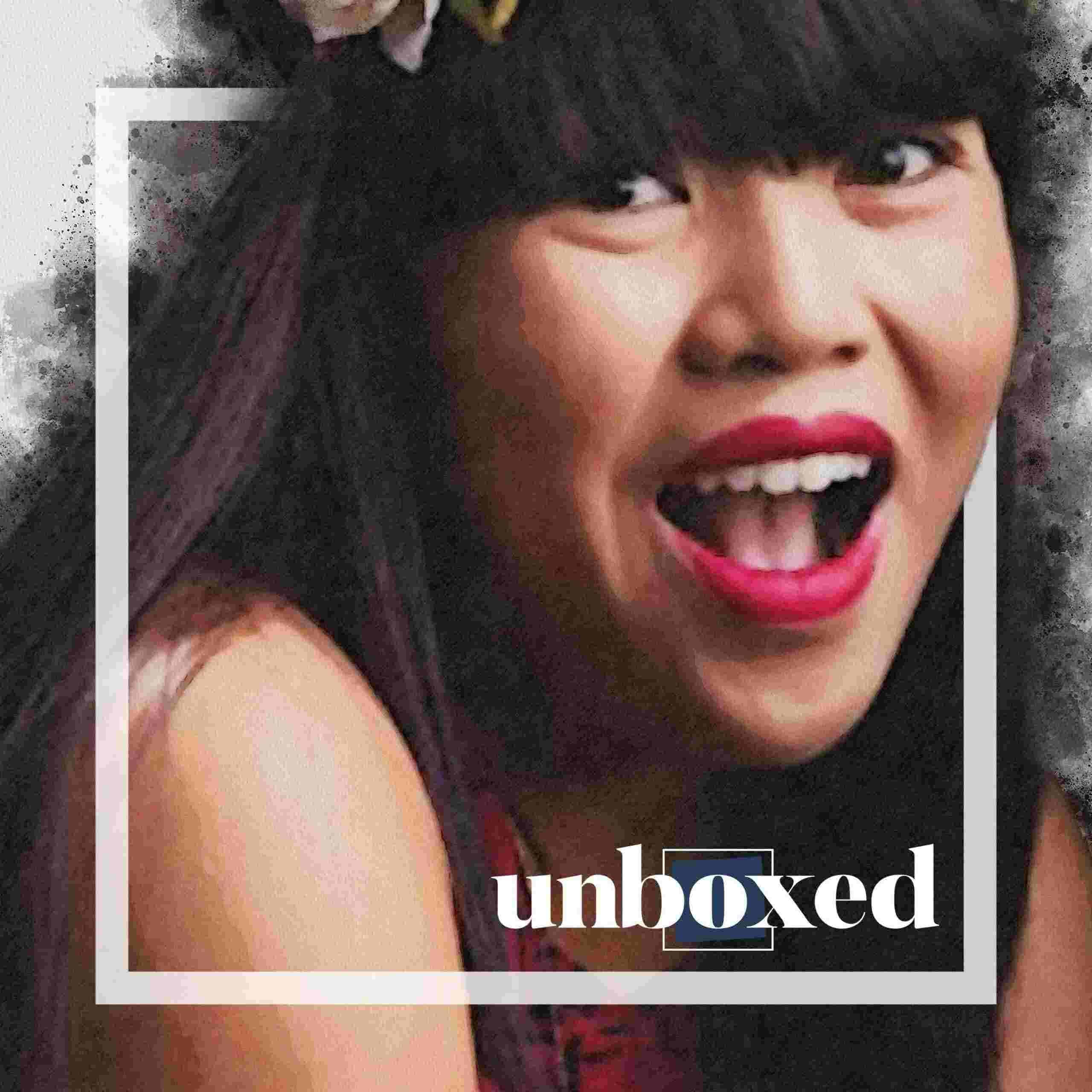 A young person with long dark hair smiles brightly, showcasing a wide grin. Theyre wearing red lipstick and a floral accessory, with the word unboxed overlaying the image—perhaps theyre preparing for one of Carol Cabreras student plays on Zoom.