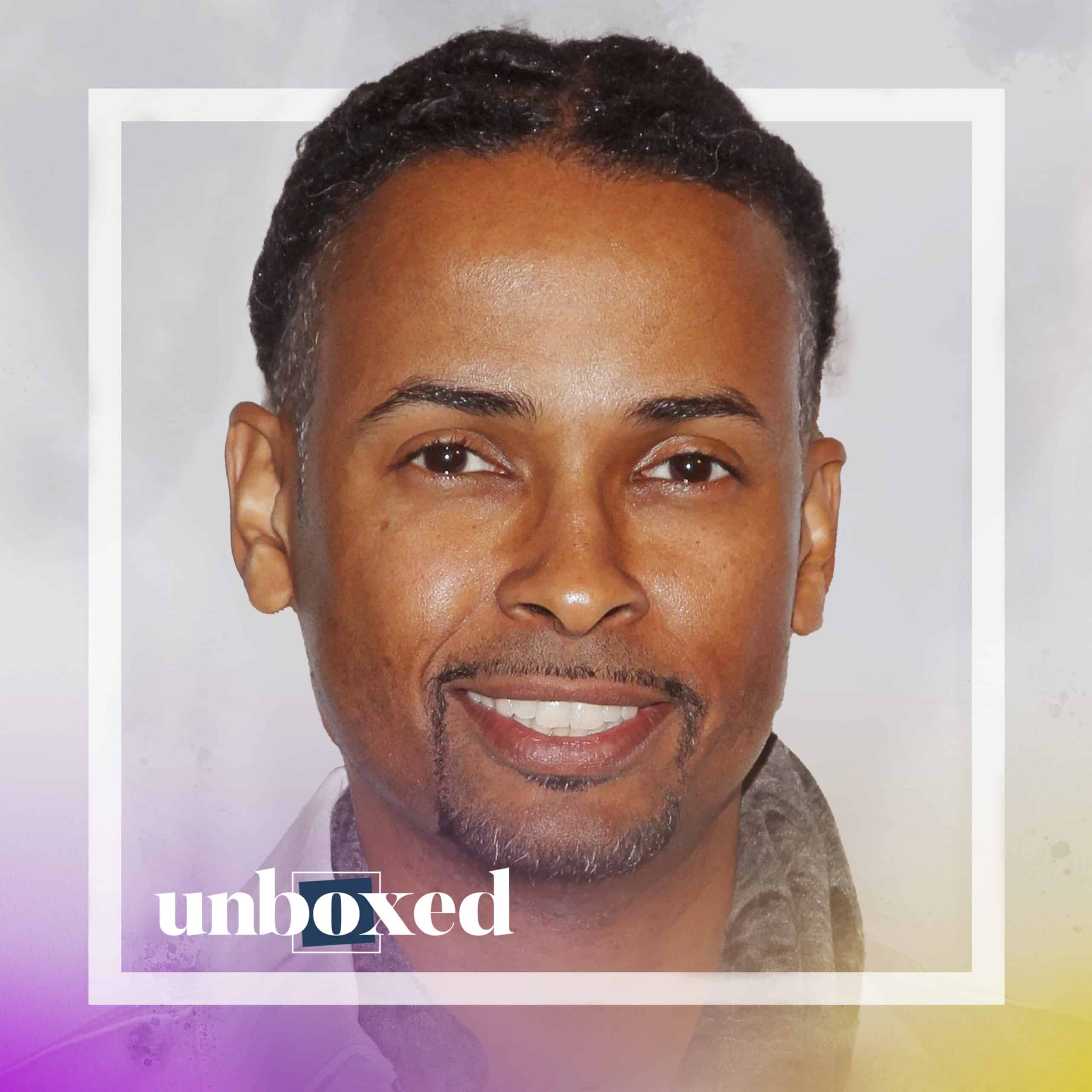 Portrait of a smiling man with braided hair and a goatee, housed in a square frame with the word unboxed at the bottom. The background blends light gray and purple hues, creating an equal balance of tones.