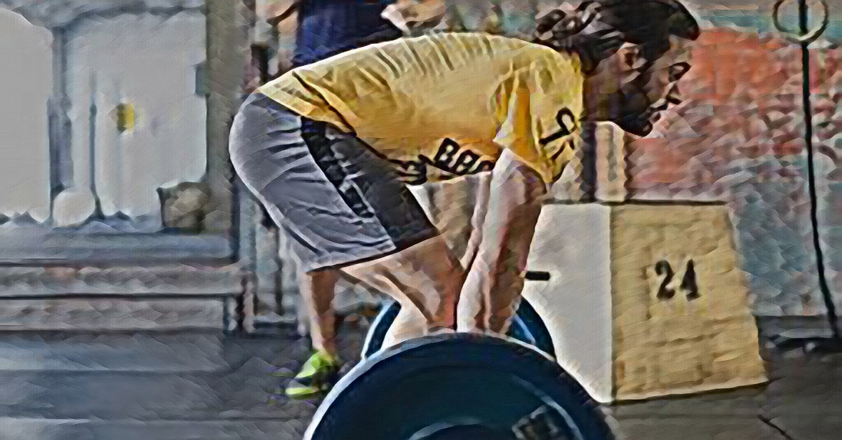 A person with long hair is showcasing their teaching skills by performing a deadlift with a barbell in a gym. They are wearing a yellow shirt and shorts, demonstrating the perfect technique. Another person and exercise equipment can be seen in the background, completing this educational scene.